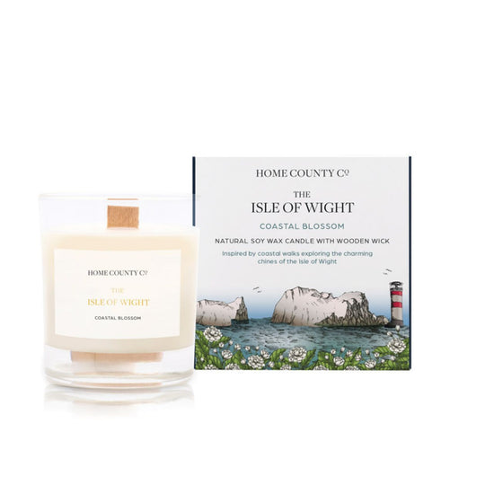 A coastal blossom scented candle from Home County Co. The wooden wick soy candle is shown next to the eco friendly candle box packaging which displays an illustration of the Isle of Wight coast and lighthouse.