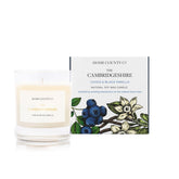 A cassis and black vanilla scented soy wax candle inspired by Cambridgeshire is shown next to its sustainable candle box with blackcurrant illustration