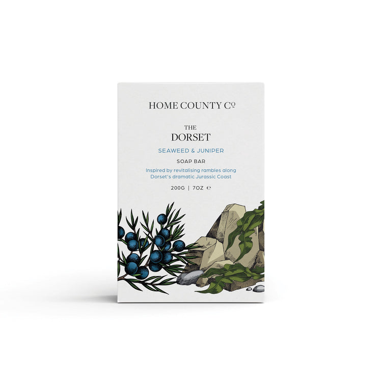 A seaweed and juniper scented natural soap bar from the Home County Co. is shown in its coastal illustrated recyclable soap bar wrap