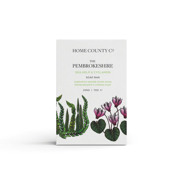 A sea kelp and cyclamen scented natural soap bar from the Home County Co. is shown in its coastal illustrated recyclable soap bar wrap