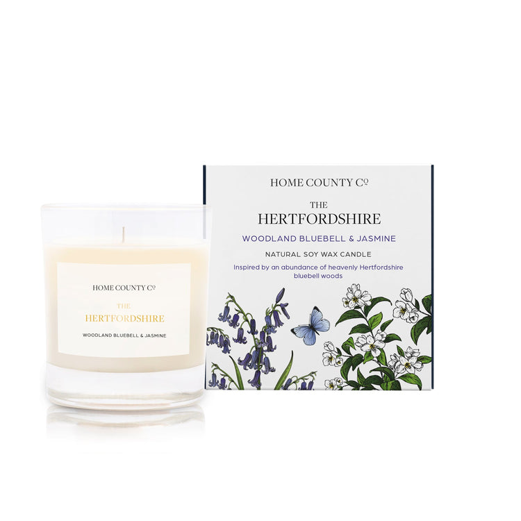 A woodland bluebell and jasmine scented soy wax candle inspired by Hertfordshire bluebell woods is shown next to its sustainable candle box with bluebell illustration