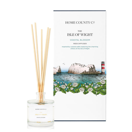A coastal blossom scented reed diffuser from Home County Co. The vegan friendly reed diffuser is shown next to the eco friendly reed diffuser box packaging featuring a coastal illustration with a lighthouse.