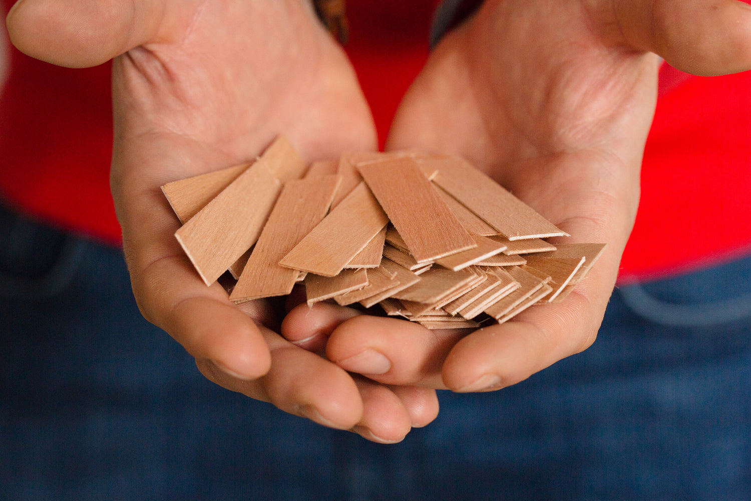 A bundle of wooden wicks is shown in the hands of a candle maker