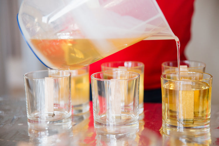 A candle maker hand-pouring soy wax wooden wick candles.