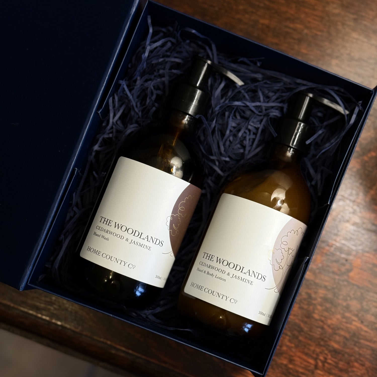 The Woodlands Cedarwood and Jasmine hand soap and lotion gift set is shown open, with the amber glass bottles on a table