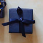 A 200g blackberry scented soy candle from the Home County Co. is shown with luxury Gift Wrap. The candle is wrapped in luxury navy wrapping paper secured with navy ribbon.