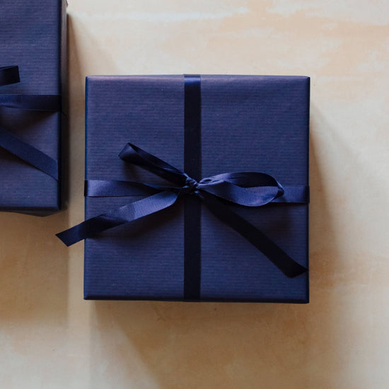 A 400g woody 3 wick soy candle from the Home County Co. is shown with luxury Gift Wrap. The 3 wick candle is wrapped in luxury navy wrapping paper secured with navy ribbon.