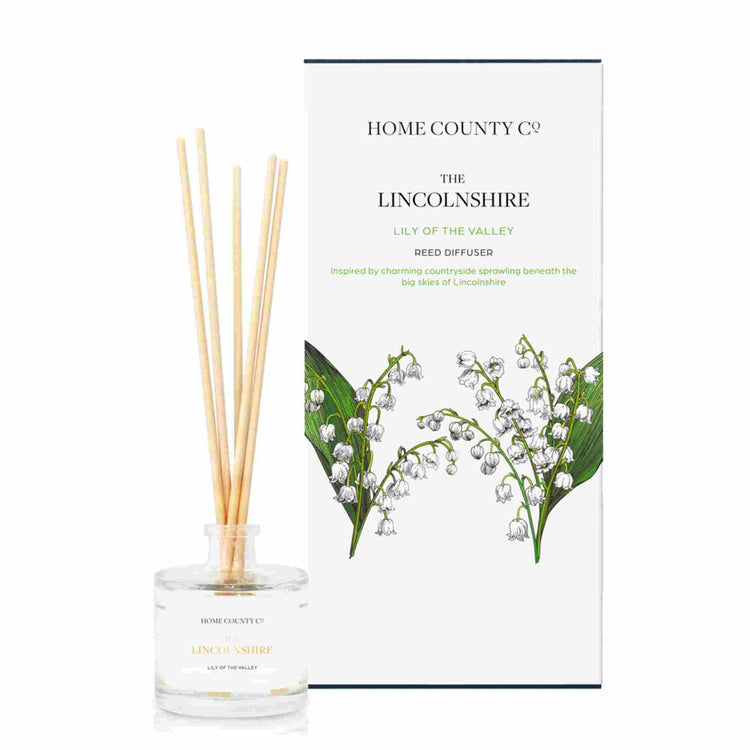 A lily of the valley scented reed diffuser from Home County Co. The vegan friendly reed diffuser is shown next to the eco friendly reed diffuser box packaging.