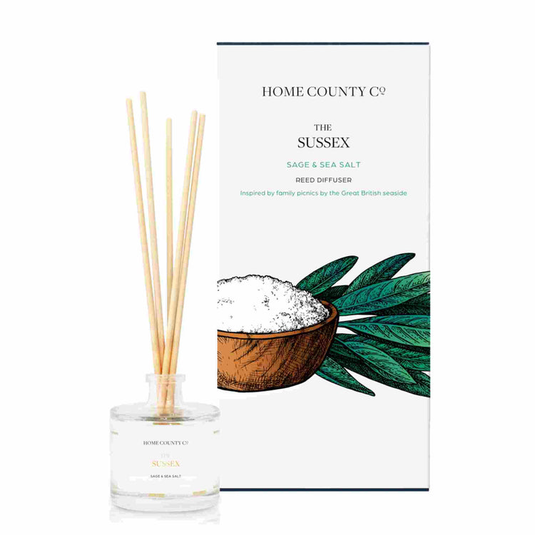 A sage and sea salt scented reed diffuser from Home County Co. The vegan friendly reed diffuser is shown next to the eco friendly reed diffuser box packaging.