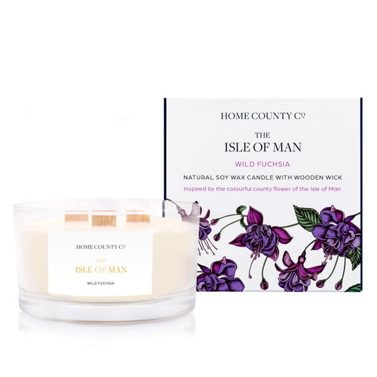 A floral scented 3 wooden wick soy candle from the Home County Co. is scented with wild fuchsia, inspired by the Isle of Man. The natural candle is shown next to its eco-friendly candle box with a floral illustration.