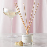 An Essex prosecco and pomelo scented reed diffuser from the Home County Co. is shown in use next to a glass of prosecco
