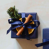 A scented 200g soy candle from the Home County Co. is shown with luxury Christmas Gift Wrap. The candle is wrapped in luxury navy wrapping paper secured with navy ribbon and Christmas embellishments.