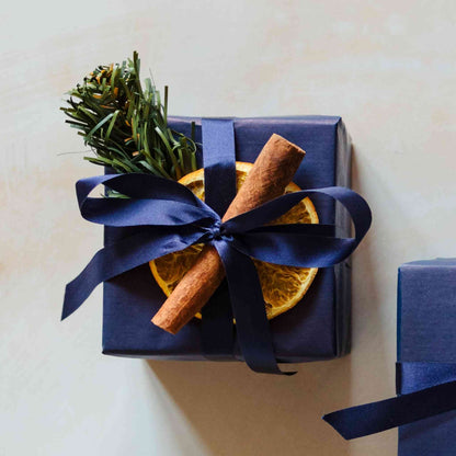 A scented 200g soy candle from the Home County Co. is shown with luxury Christmas Gift Wrap. The candle is wrapped in luxury navy wrapping paper secured with navy ribbon and Christmas embellishments.