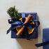 A scented 200g soy candle from the Home County Co. is shown with luxury Christmas Gift Wrap. The candle is wrapped in luxury navy wrapping paper secured with navy ribbon and Christmas embellishments.