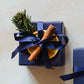 A 200g linen scented soy candle from the Home County Co. is shown with luxury Christmas Gift Wrap. The candle is wrapped in luxury navy wrapping paper secured with navy ribbon and Christmas embellishments.