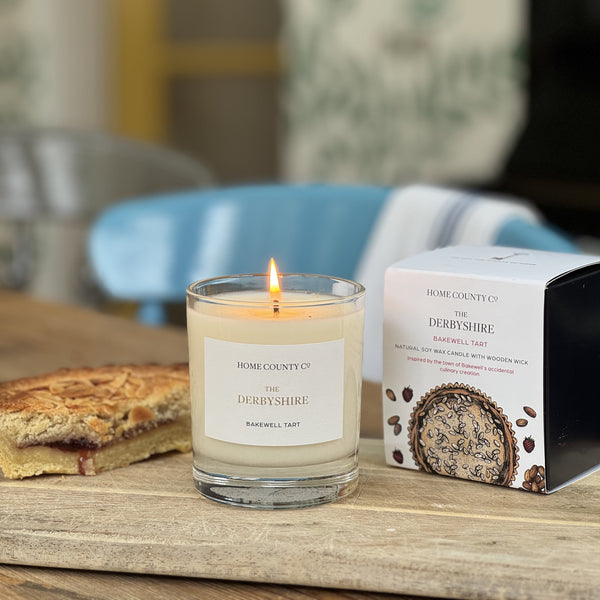 Candle with a lit wick on a wooden surface next to a box labeled 'Derbyshire'.