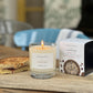 Candle with a lit wick on a wooden surface next to a box labeled &
