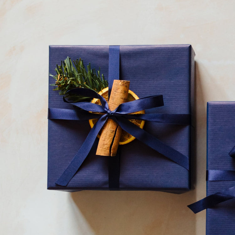 A 400g linen scented 3 wick soy candle from the Home County Co. is shown with luxury Christmas Gift Wrap. The 3 wick candle is wrapped in luxury navy wrapping paper secured with navy ribbon and Christmas embellishments.