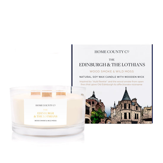 A wood smoke scented 3 wooden wick soy candle from the Home County Co. is inspired by Edinburgh and The Lothians, shown next to its eco friendly candle box.