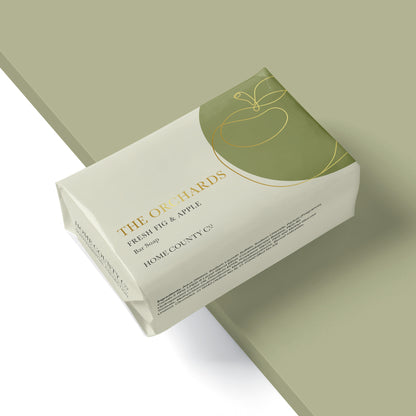 A fruity fresh fig and apples scented soap bar from the Home County Co. is shown wrapped in a luxury soap wrap with gold foil apple illustration