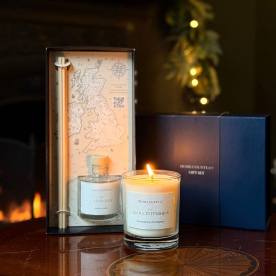 A Home County Co. Candle and Reed Diffuser Gift Set is shown in front of an open fire with the luxury navy gift box