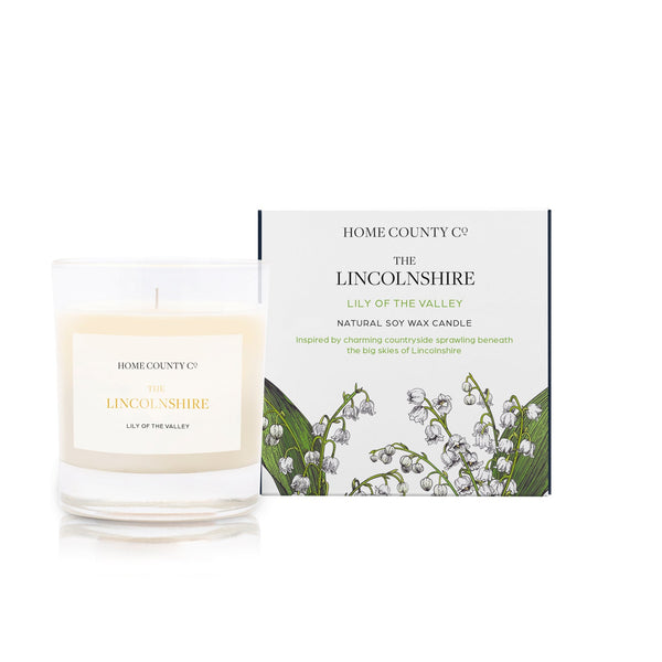 A lily of the valley scented soy wax candle inspired by Lincolnshire is shown next to its sustainable candle box with lily of the valley illustration