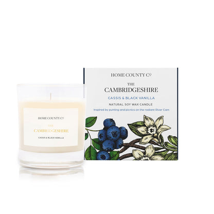 A cassis and black vanilla scented soy wax candle inspired by Cambridgeshire is shown next to its sustainable candle box with blackcurrant illustration