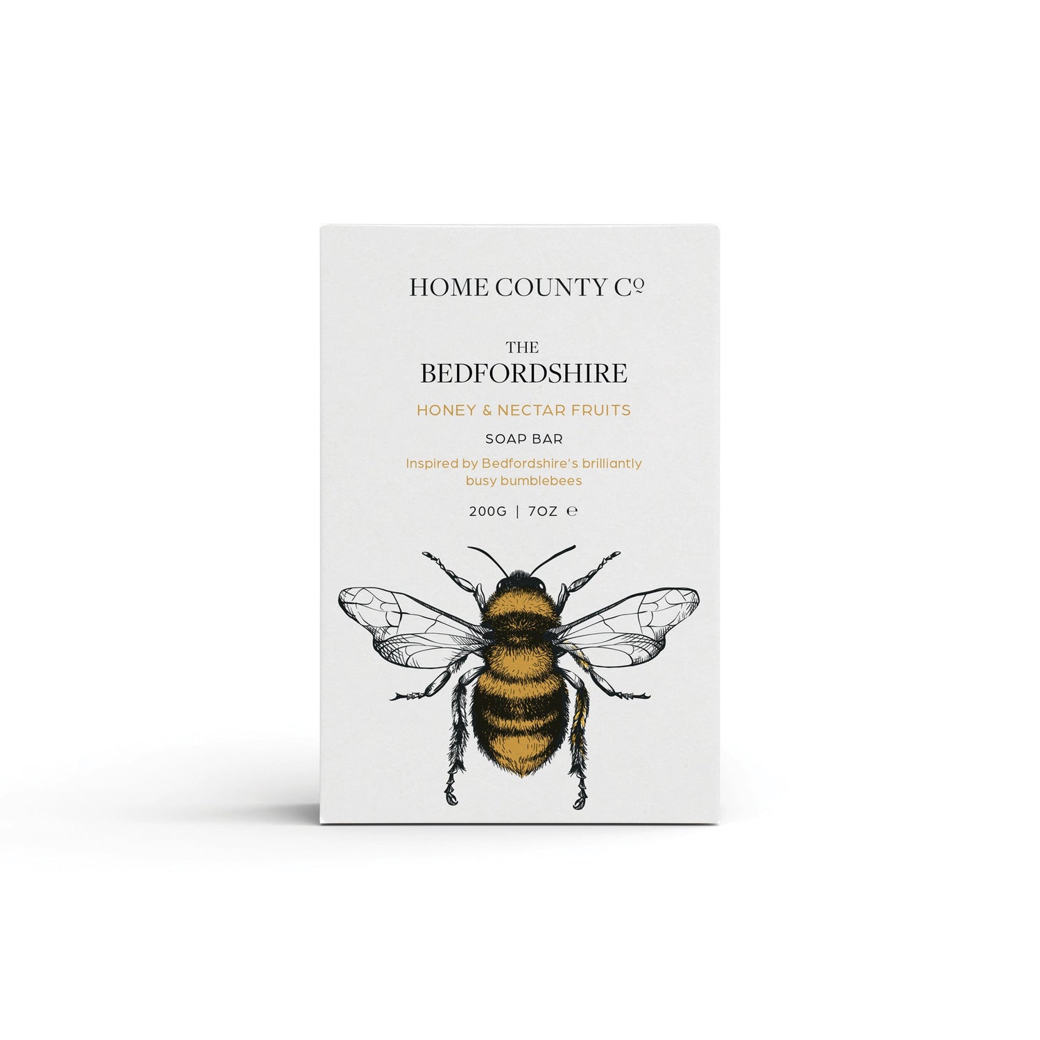 A honey scented natural soap bar from the Home County Co. is shown in its honey bee illustrated recyclable soap bar wrap