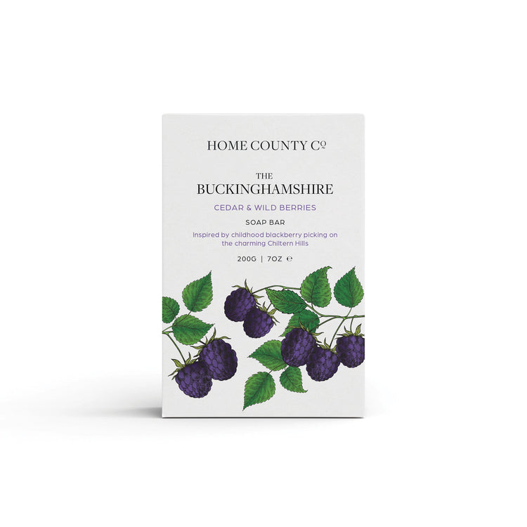 A blackberry and bay scented natural soap bar from the Home County Co. is shown in its berry illustrated recyclable soap bar wrap