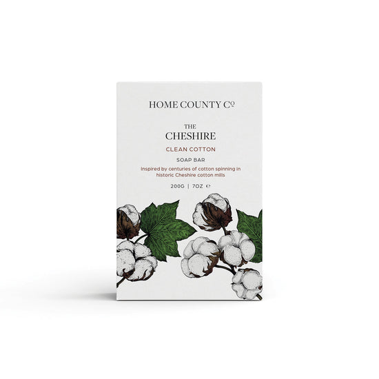 A clean cotton scented natural soap bar from the Home County Co. is shown in its cotton illustrated recyclable soap bar wrap