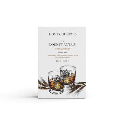 An Irish Whiskey scented natural soap bar from the Home County Co. is shown in its whiskey illustrated recyclable soap bar wrap