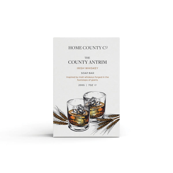 An Irish Whiskey scented natural soap bar from the Home County Co. is shown in its whiskey illustrated recyclable soap bar wrap