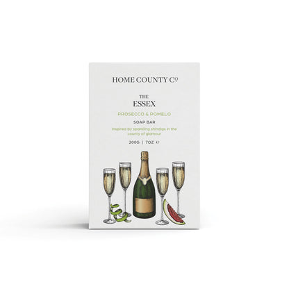 A prosecco scented natural soap bar from the Home County Co. is shown in its prosecco illustrated recyclable soap bar wrap