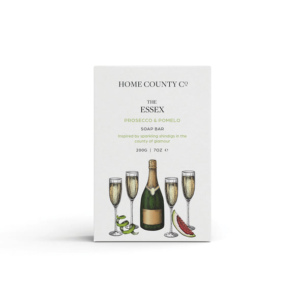 A prosecco scented natural soap bar from the Home County Co. is shown in its prosecco illustrated recyclable soap bar wrap