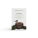 A rosewood and velvet moss woody scented natural soap bar from the Home County Co. is shown in its woodland illustrated recyclable soap bar wrap