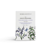 A bluebell scented natural soap bar from the Home County Co. is shown in its bluebell illustrated recyclable soap bar wrap