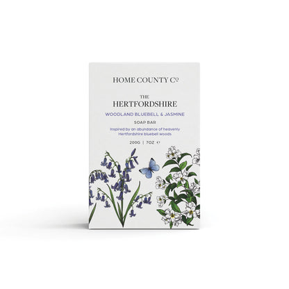 A bluebell scented natural soap bar from the Home County Co. is shown in its bluebell illustrated recyclable soap bar wrap