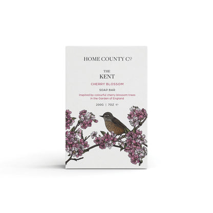 A cherry blossom floral scented natural soap bar from the Home County Co. is shown in its cherry blossom illustrated recyclable soap bar wrap