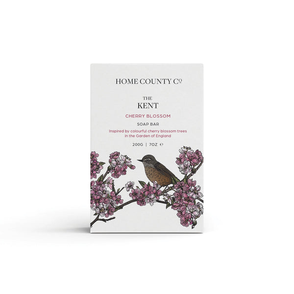 A cherry blossom floral scented natural soap bar from the Home County Co. is shown in its cherry blossom illustrated recyclable soap bar wrap