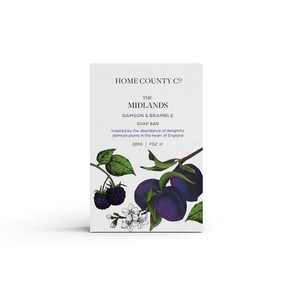 A plum scented natural soap bar from the Home County Co. is shown in its plum illustrated recyclable soap bar wrap