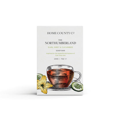 An earl grey and cucumber scented natural soap bar from the Home County Co. is shown in its earl grey tea illustrated recyclable soap bar wrap