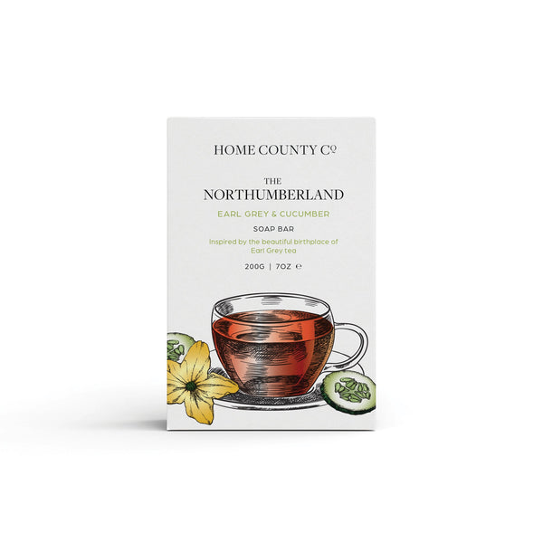 An earl grey and cucumber scented natural soap bar from the Home County Co. is shown in its earl grey tea illustrated recyclable soap bar wrap