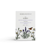 An english lavender and chamomile scented natural soap bar from the Home County Co. is shown in its lavender illustrated recyclable soap bar wrap