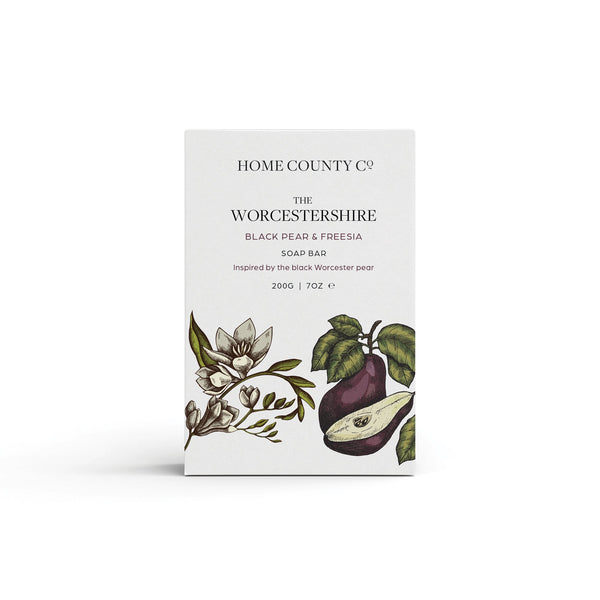 A pear and freesia scented natural soap bar from the Home County Co. is shown in its pear illustrated recyclable soap bar wrap