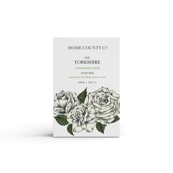 A Yorkshire Rose scented natural soap bar from the Home County Co. is shown in its white rose illustrated recyclable soap bar wrap