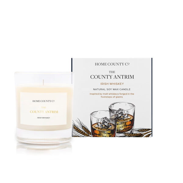 An Irish whiskey scented soy wax candle inspired by County Antrim is shown next to its sustainable candle box with whiskey illustration