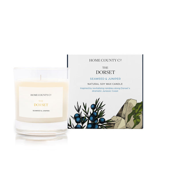 A seaweed and junipers scented soy wax candle inspired by Dorset is shown next to its sustainable candle box with coastal illustration