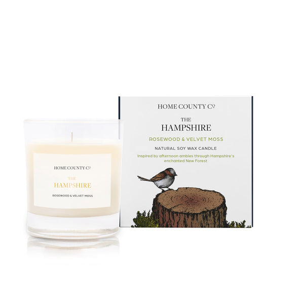 A rosewood and velvet moss scented soy wax candle inspired by Hampshire's New Forest is shown next to its sustainable candle box with woodland illustration