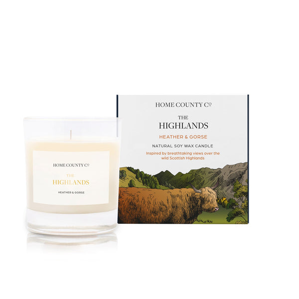 A heather and gorse scented soy wax candle inspired by the Scottish Highlands is shown next to its sustainable candle box with Highland cow illustration