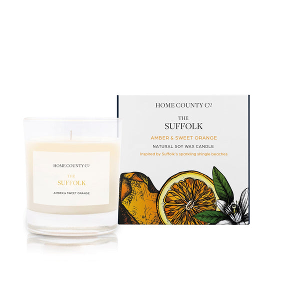 An amber and sweet orange scented soy wax candle inspired by Suffolk is shown next to its sustainable candle box with orange illustration